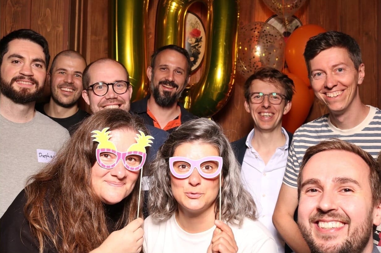 9 people posing for a photoin front of golden baloons with the number 10