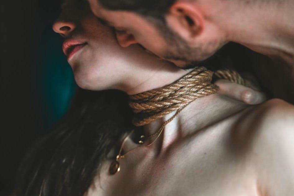 Intimate moment with rope wrapped around her neck as he kisses her skin, capturing the sensuality, trust, and erotic tension of rope play and light breath control.