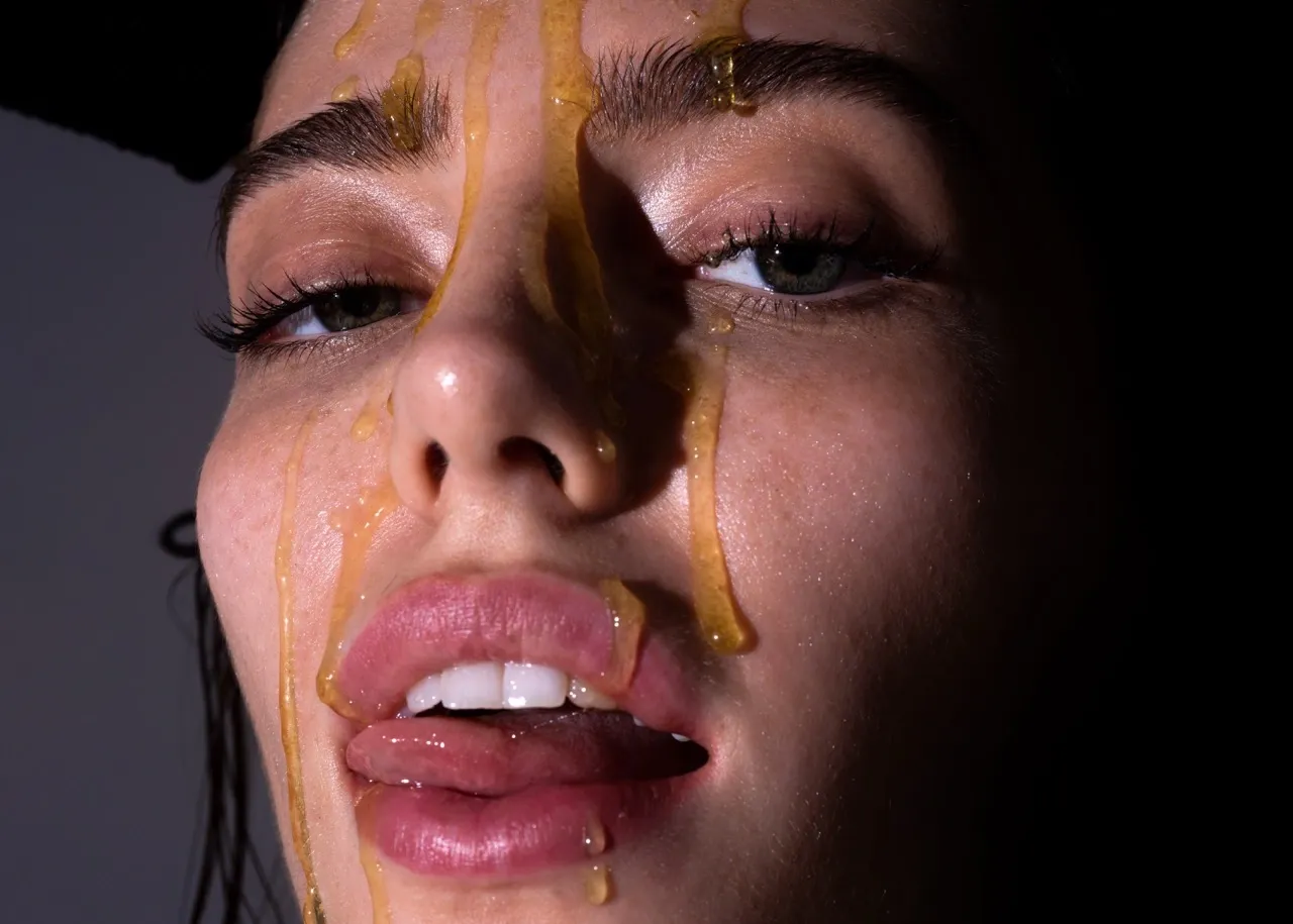 Sensual close-up of a woman’s face with honey dripping down, capturing sweet temptation and raw desire.
