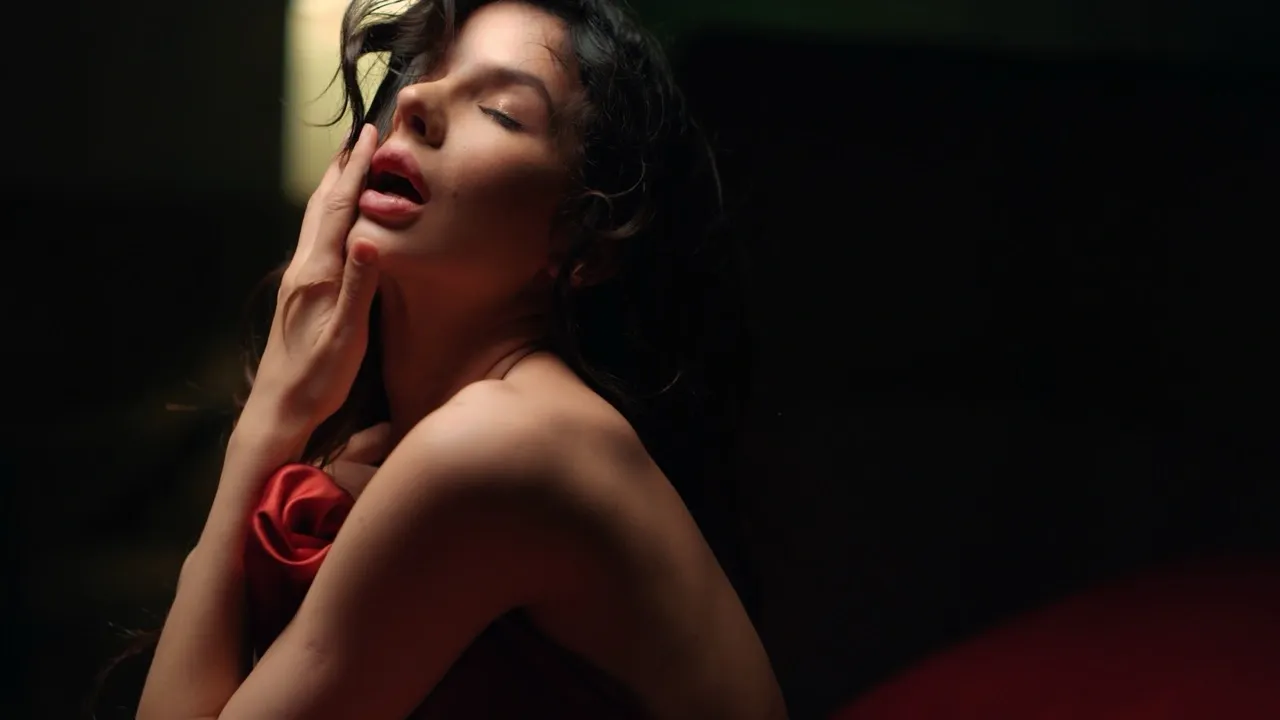 Sensual woman in red lingerie posing with eyes closed, hand gently touching her neck during boudoir photoshoot