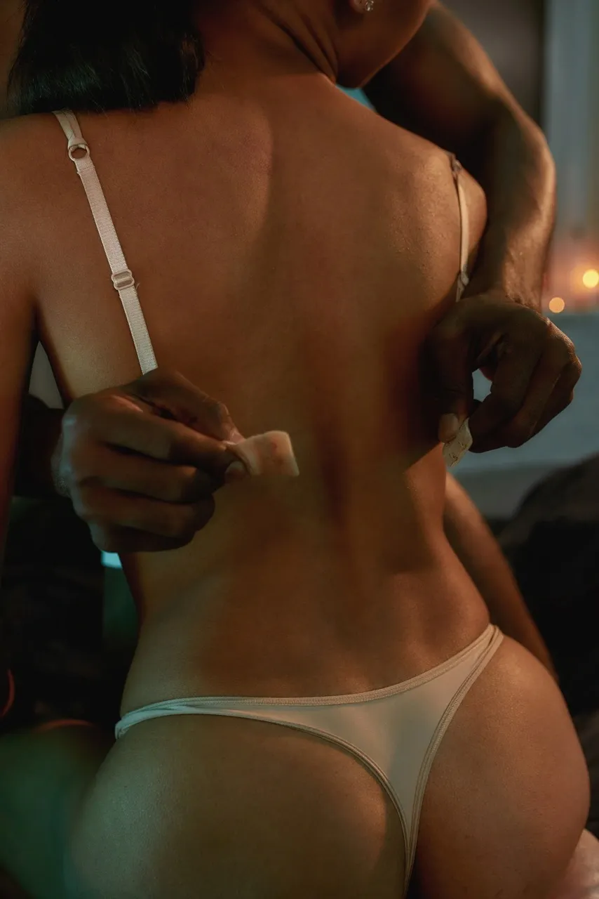 Man’s hands slowly unfastening woman’s white bra from behind during intimate boudoir session