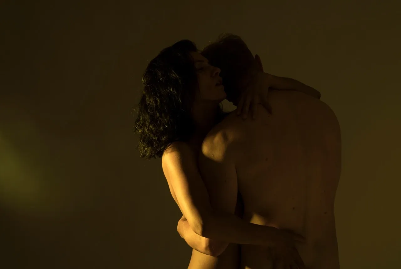 Passionate couple embracing in dim light, woman’s arms wrapped around man’s back in intimate moment during a boudoir photo session