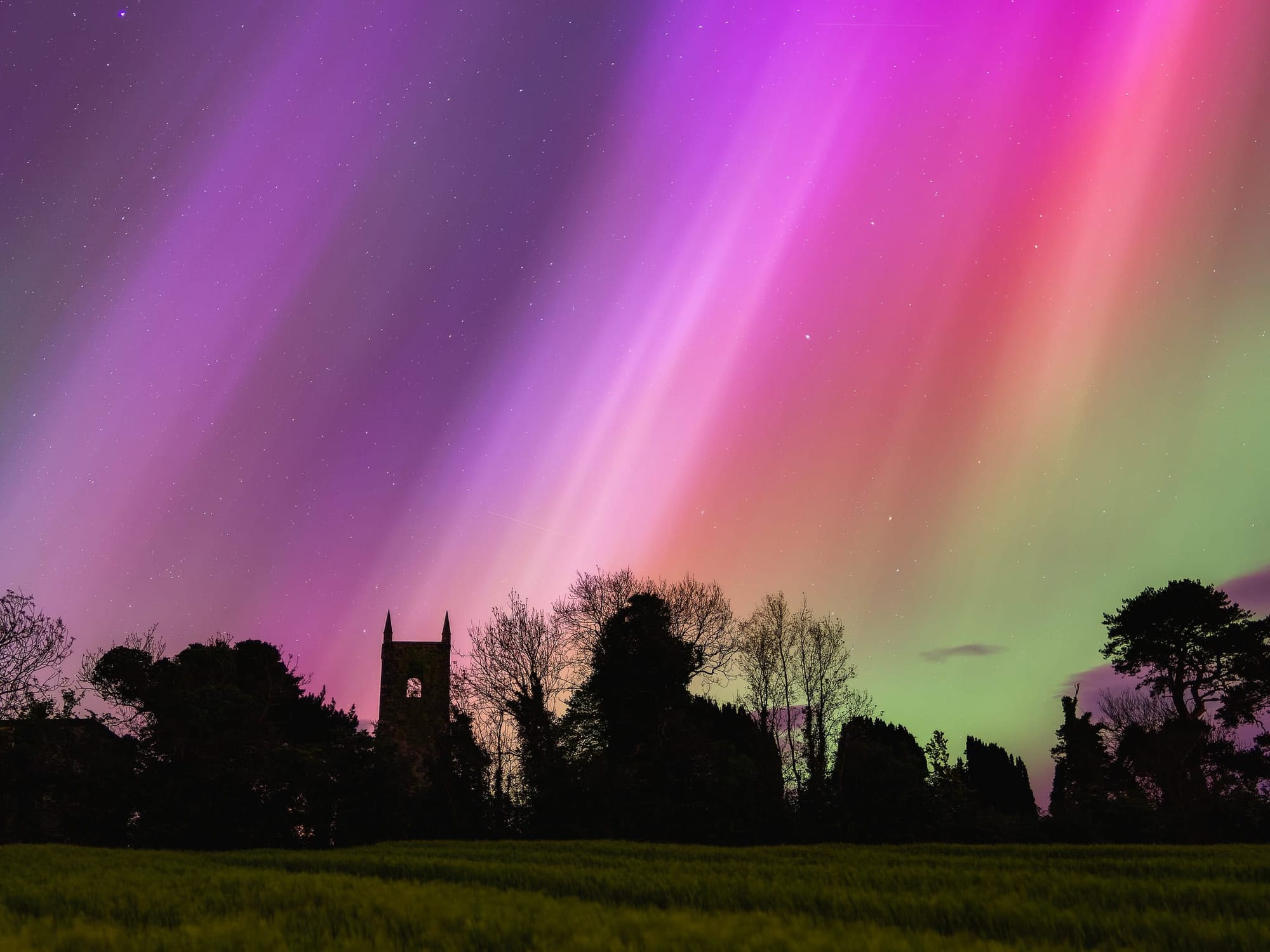 Multicoloured beams reaching down to a silhouetted church tower. Stars shining through the coloured light.