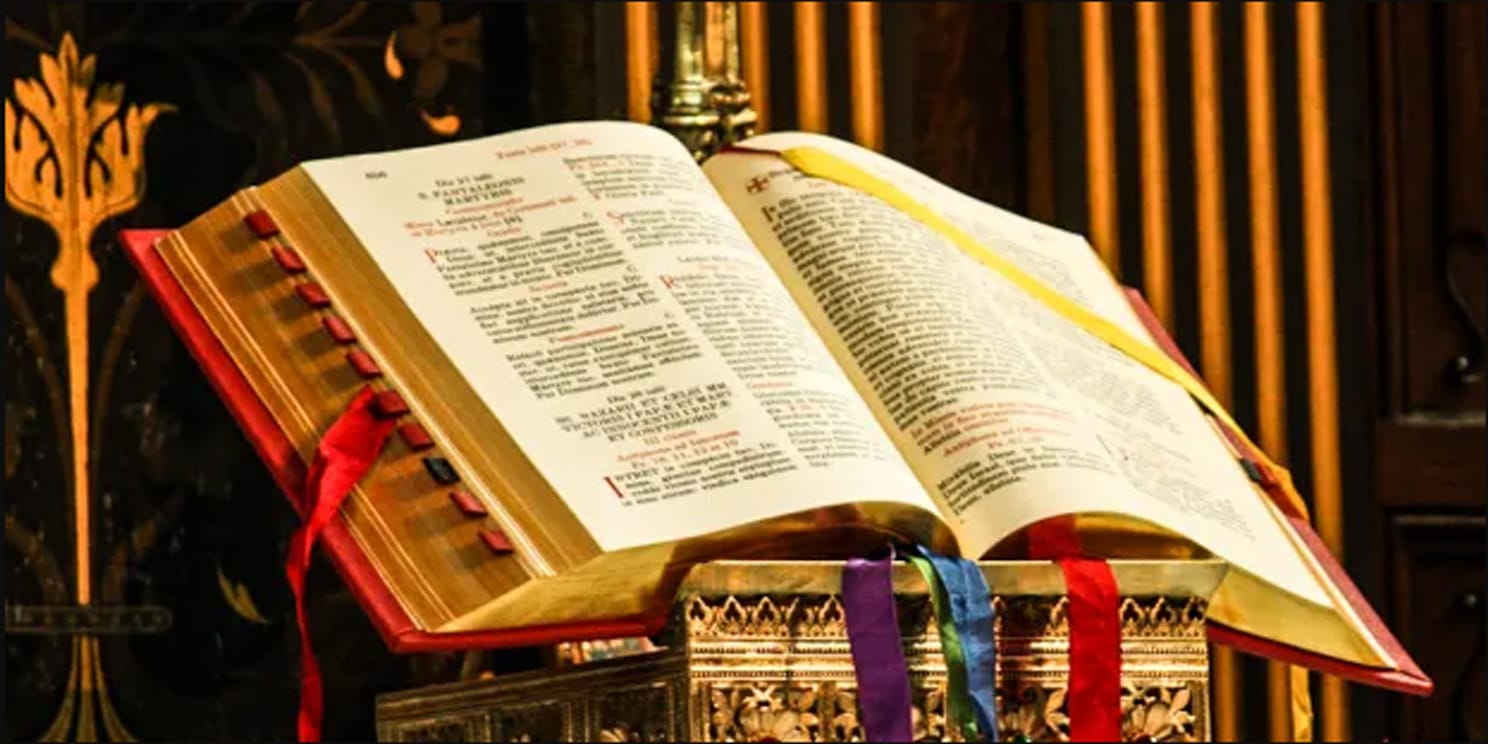 Photo of an open Lectionary with colored ribbons on a stand in a church.