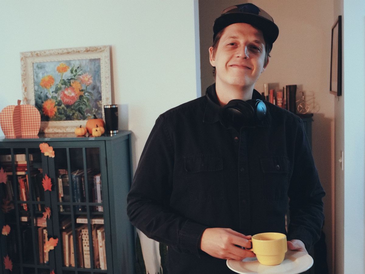 Young man in front of a bookcase at the Covenant Church meeting holding a yellow cup of tea and saucer