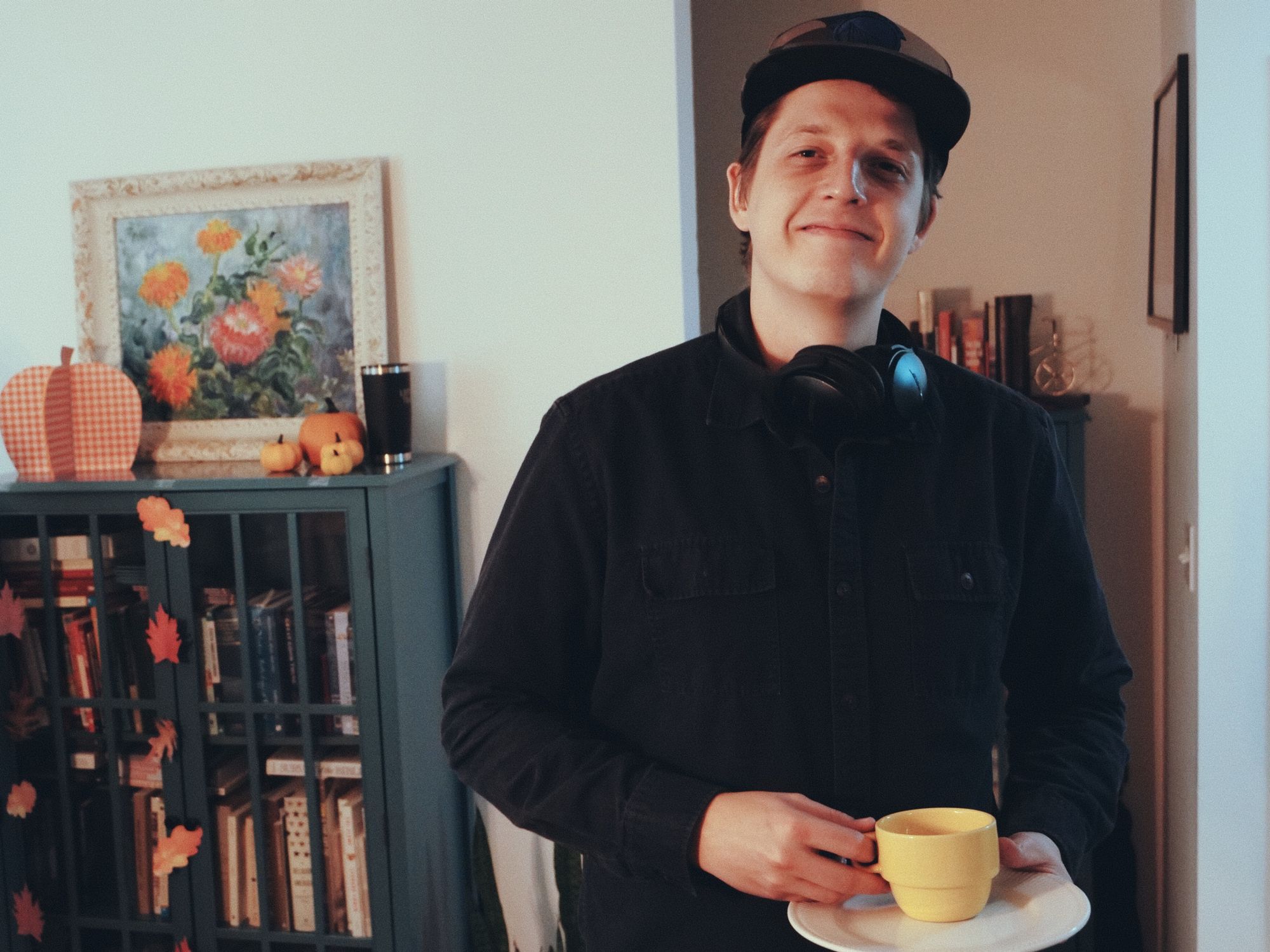 Young man in front of a bookcase at the Covenant Church meeting holding a yellow cup of tea and saucer