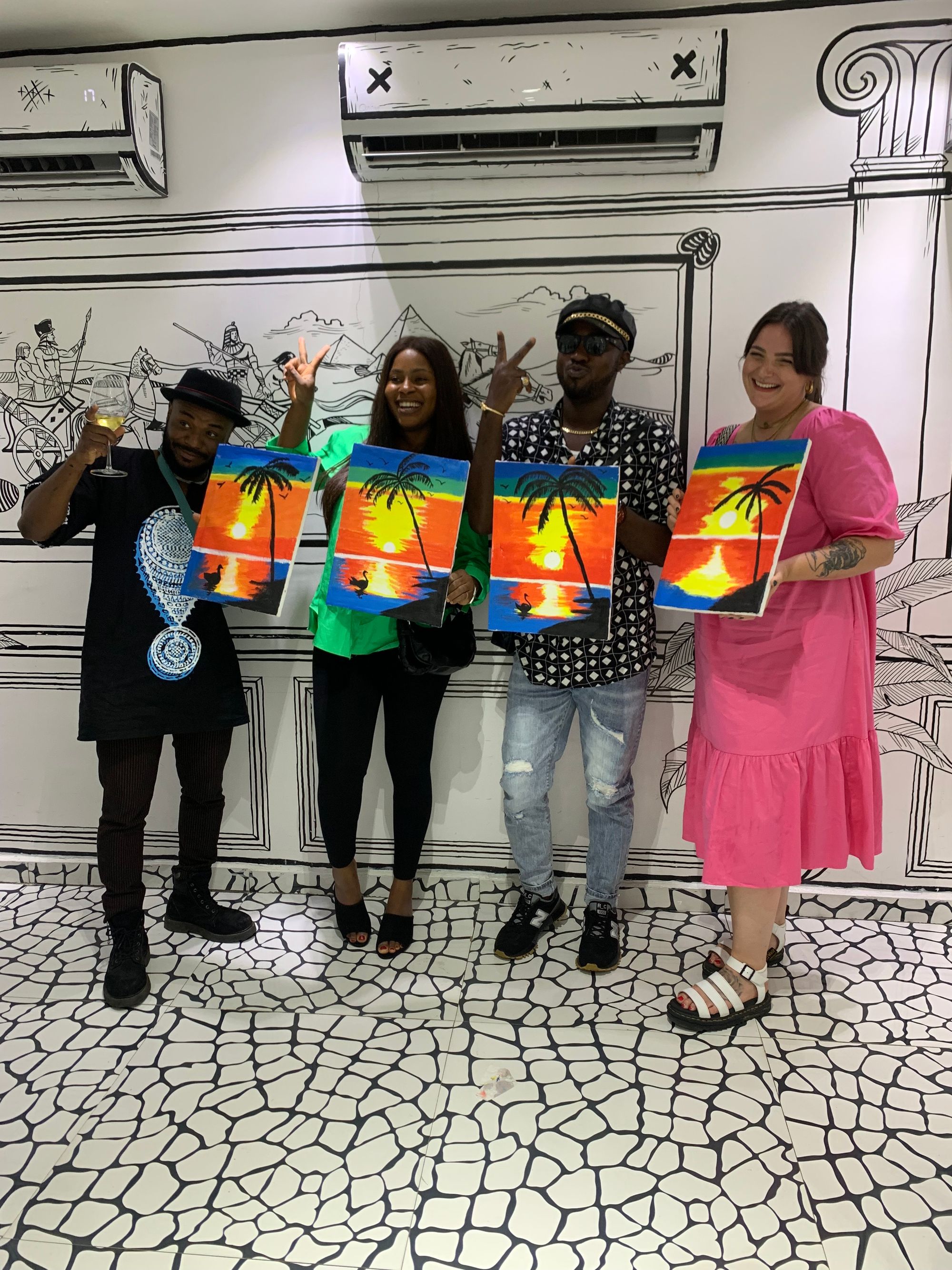 Attendees holding their final paintings and smiling at a Sip and Paint NG session