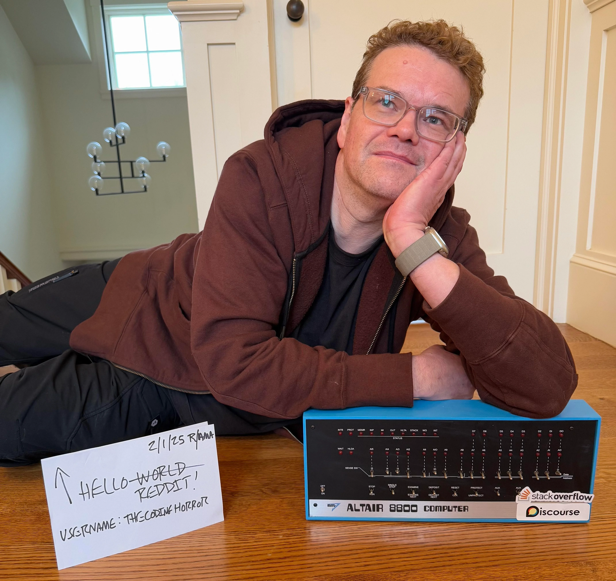 Jeff Atwood inside home laying on the floor, leaning on an Altair 8800 reproduction with StackOverflow and Discourse stickers, next to a piece of paper with "2/1/25 R/AMA, Hello Reddit!, username: thecodinghorror" which is required to validate guests on the subreddit r/ama