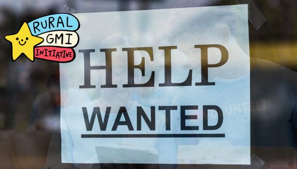 A photo of a help wanted sign taped to a window. In the reflection of the window are two volunteers, working together. The RGMII logo is included in the image.