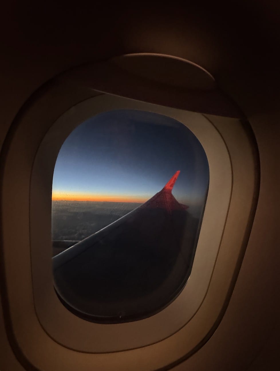 A wingtip over cloud at sunrise, photographed from a passenger window