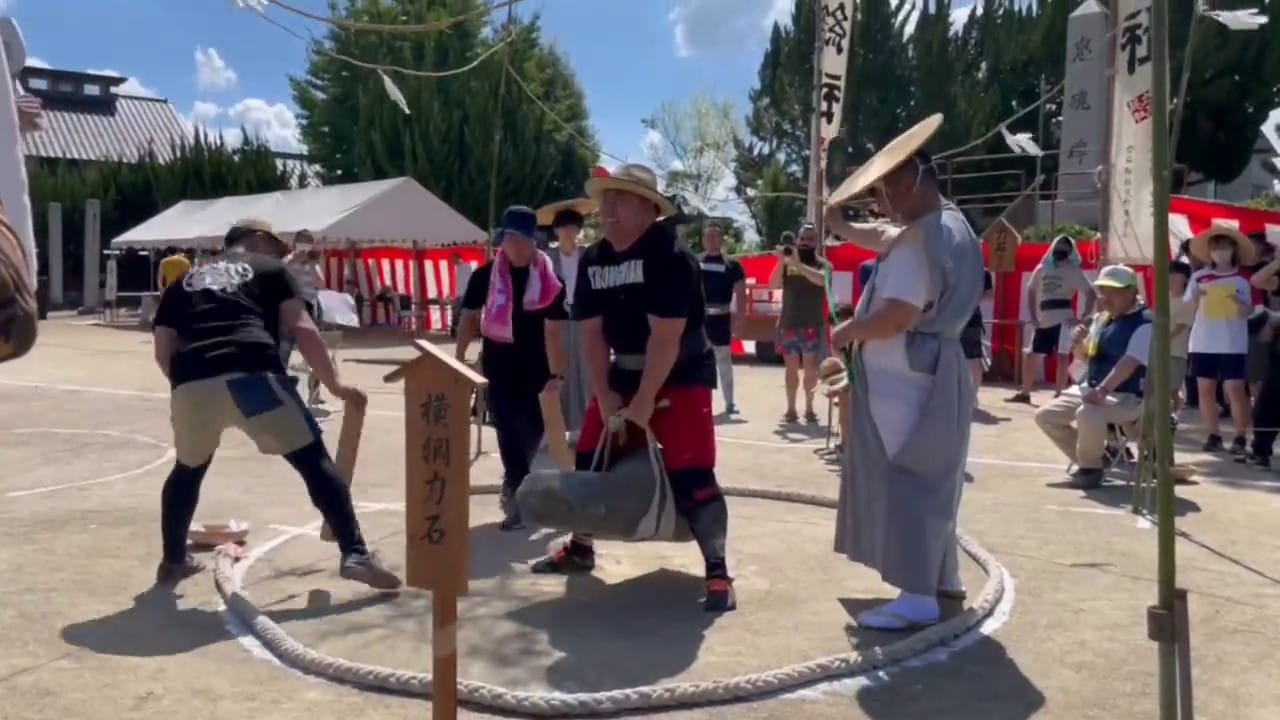 A Japanese Strongman lifts a stone using a harness in a mini dohyo.