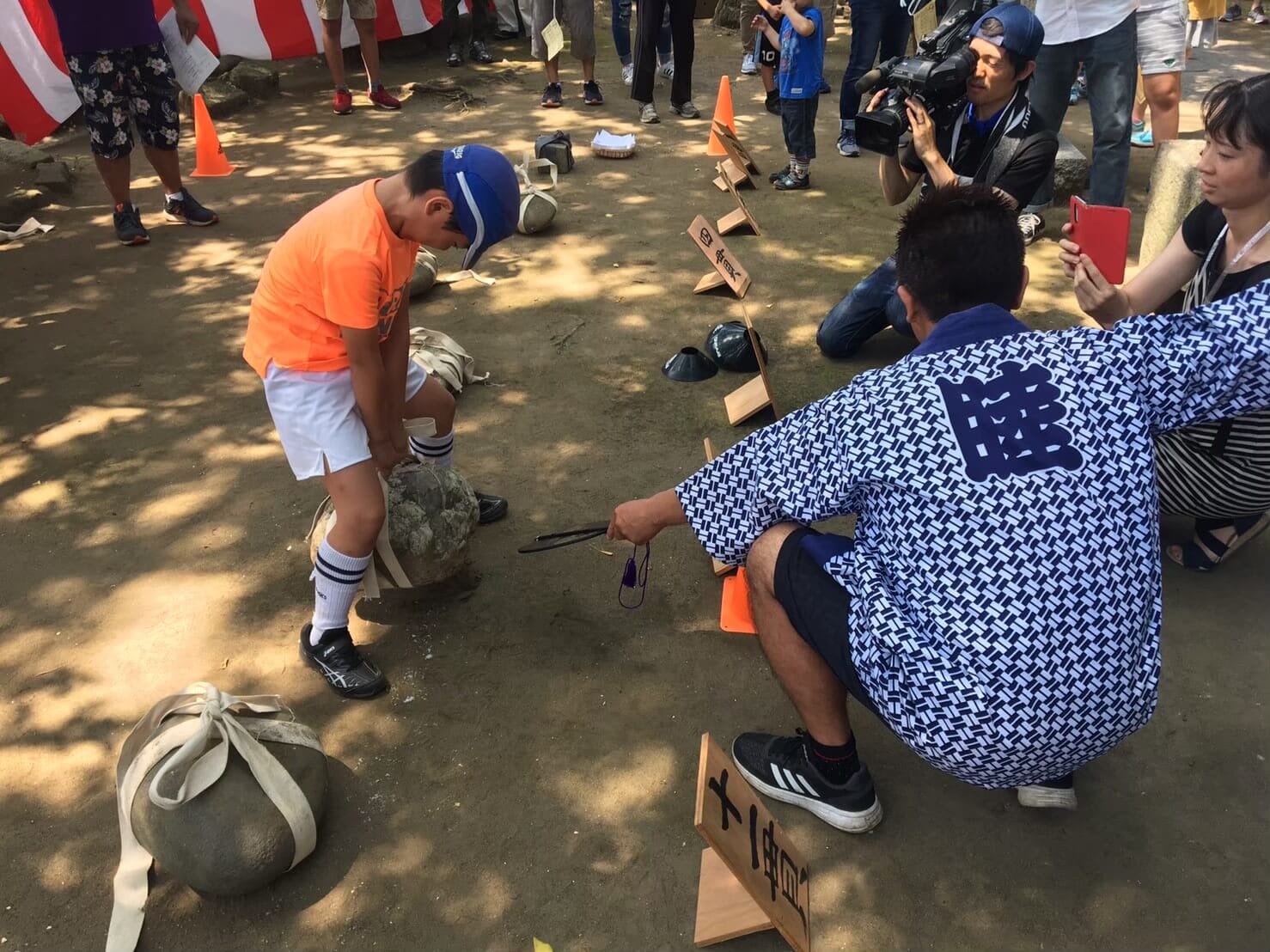 A young boy lifts a stone from the floor using a harness wrapped around the stone.
