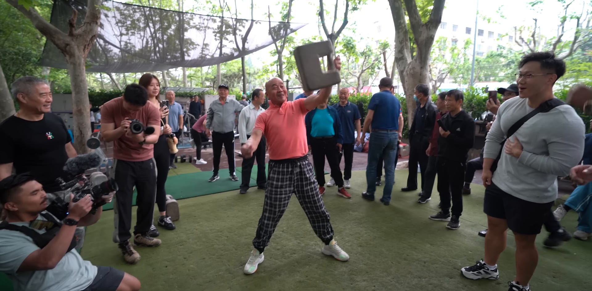 A chinese man swings a stone lock into the air.