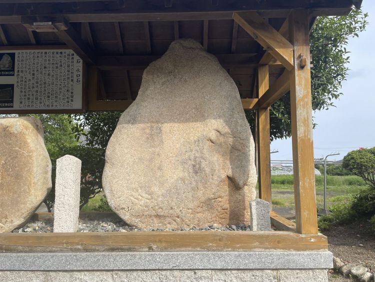A towering, almost tear-drop shaped, slab stands on a waist-height display. The structure has a roof to cover the stone.