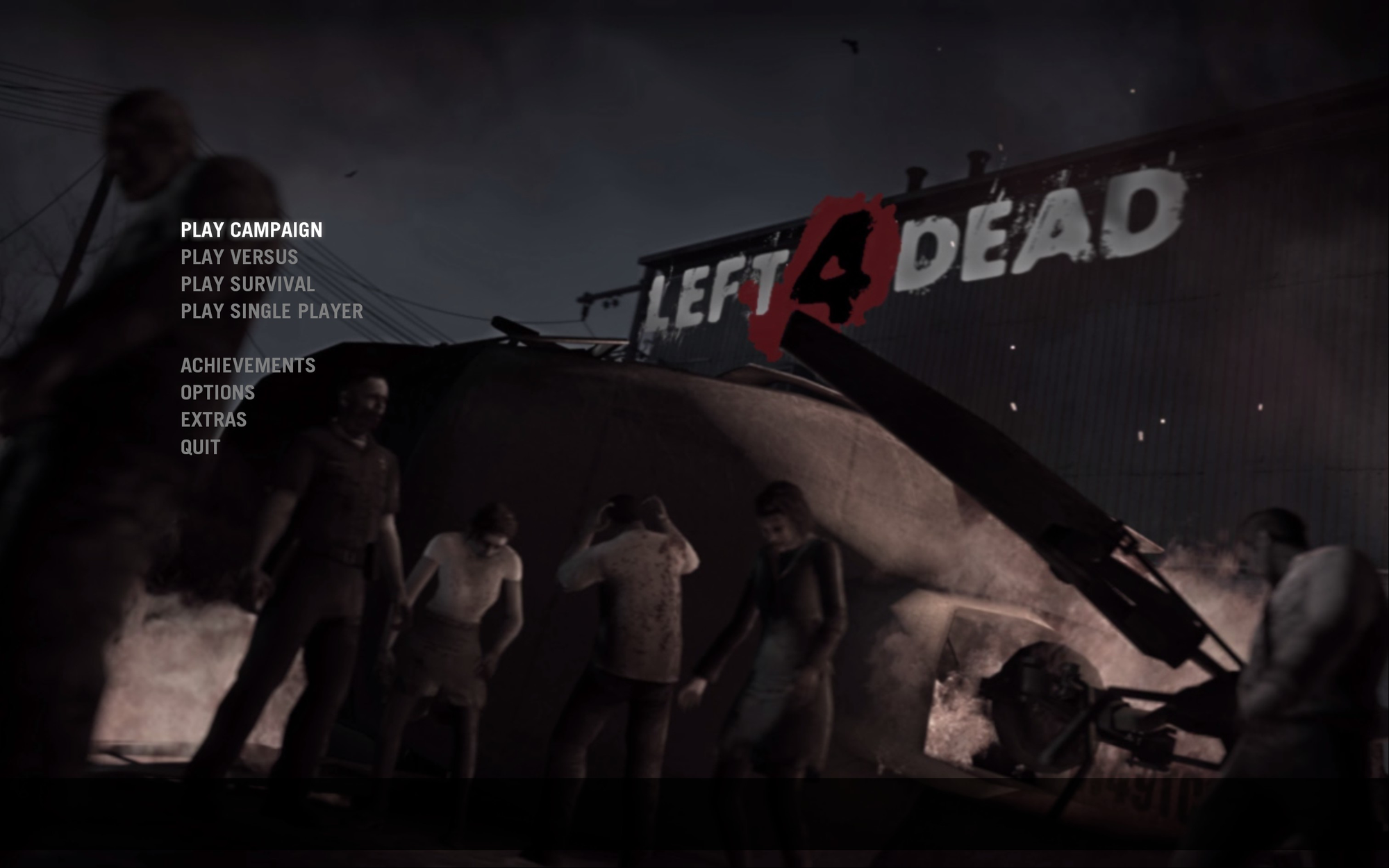 The menu screen of Left 4 Dead. Its background features a helicopter wreck surrounded by zombies, and the game's logo is diegetically placed in a building in the background.
