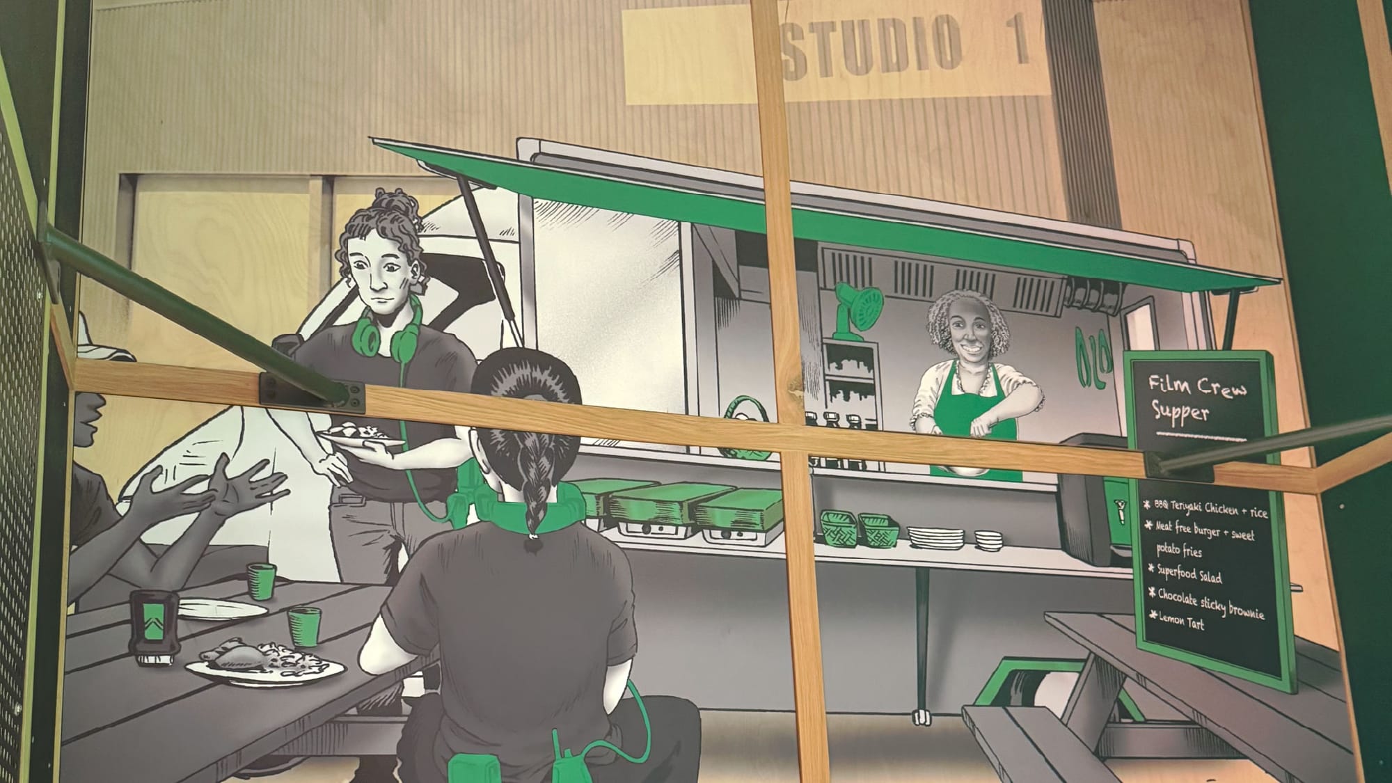 An illustration on one of the walls showing a film crew on a break. There's three crew members around a table, a lady preparing food inside a truck, and a sign reading "Film Crew Supper".