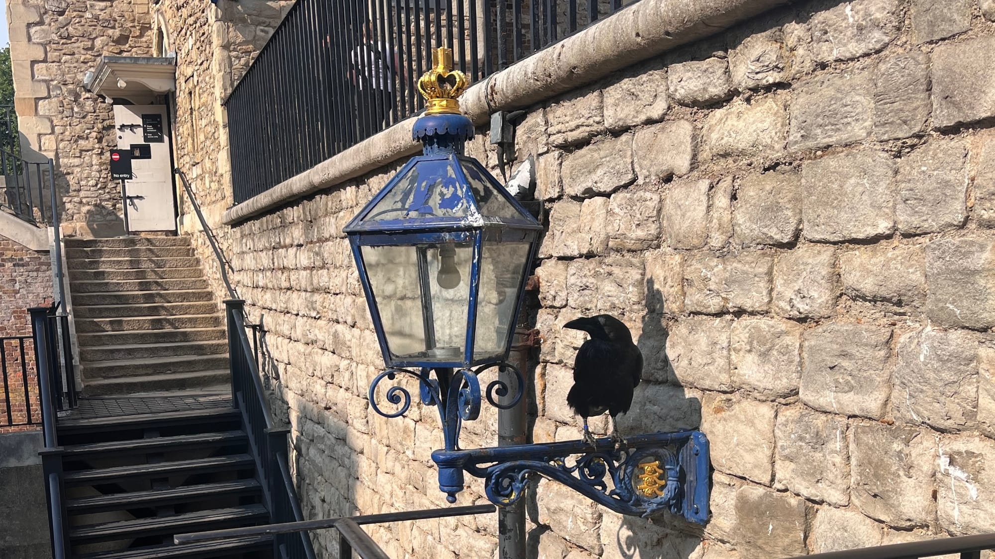 A Raven on top of a lamp on a wall in the Tower of London.