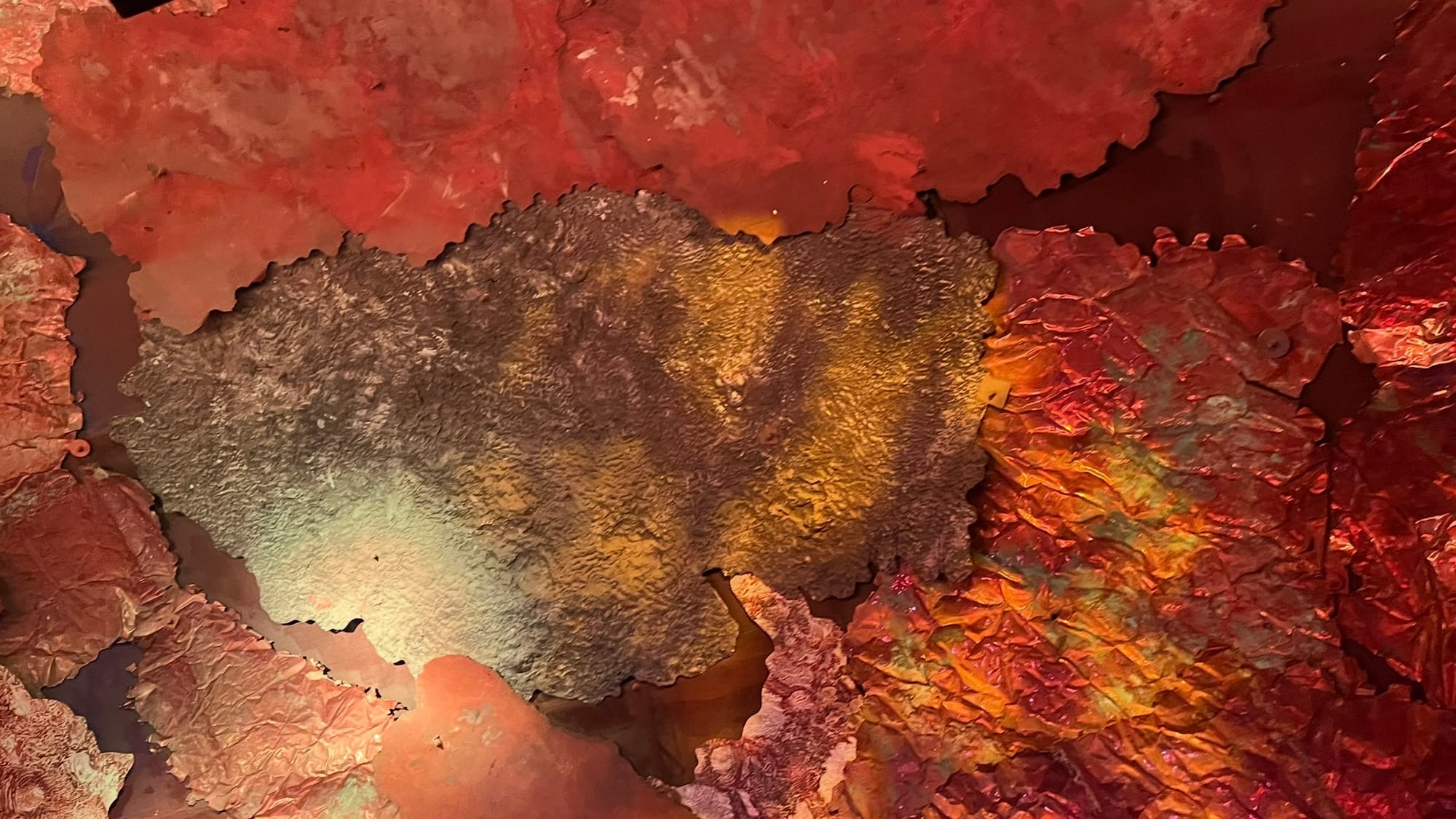 Some of the wall inside the escalator. It's lined with sheets of rocks and lit up with red, orange, and yellow lights.