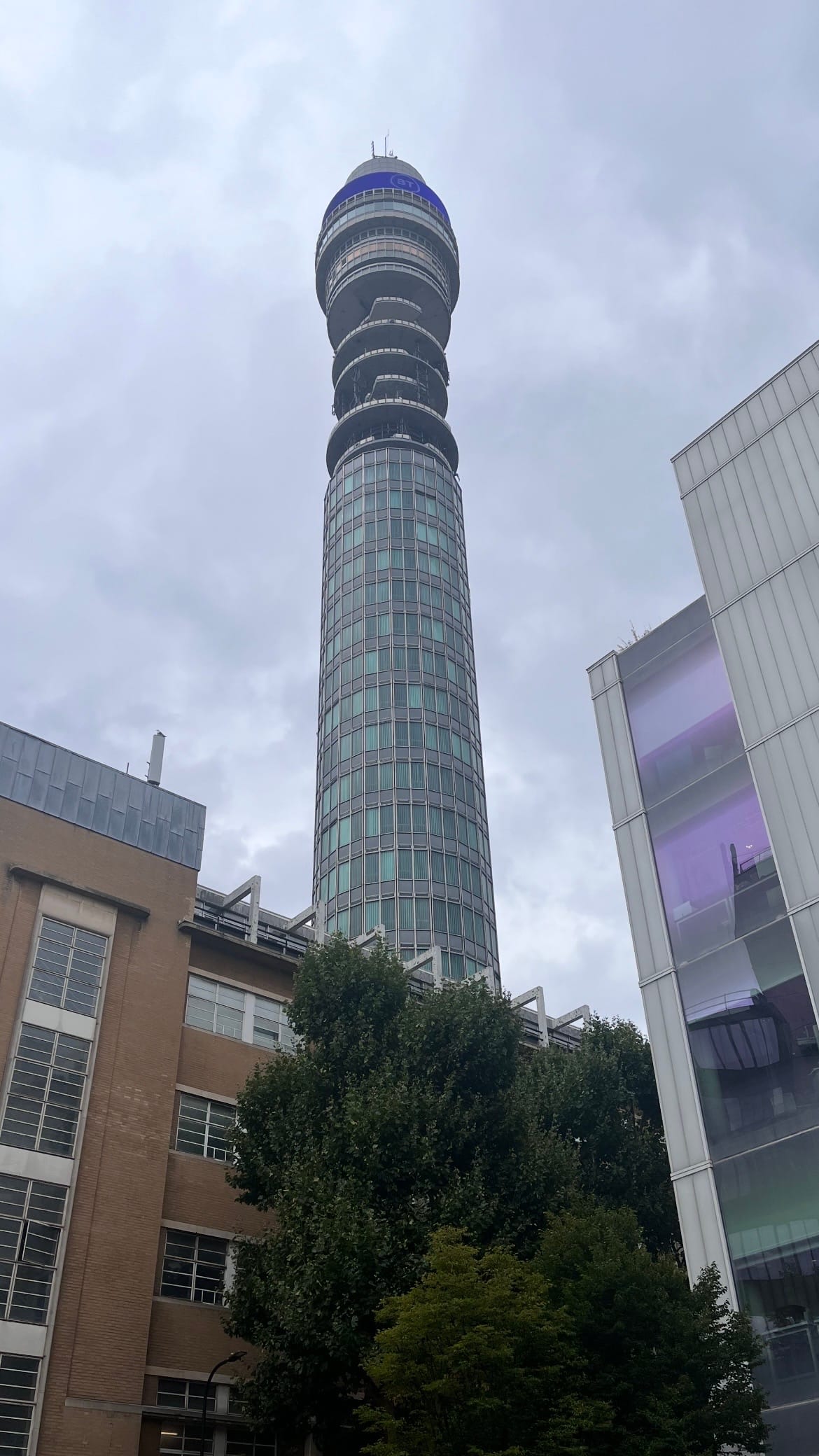 A vertical view of the BT Tower, towering over every building nearby.