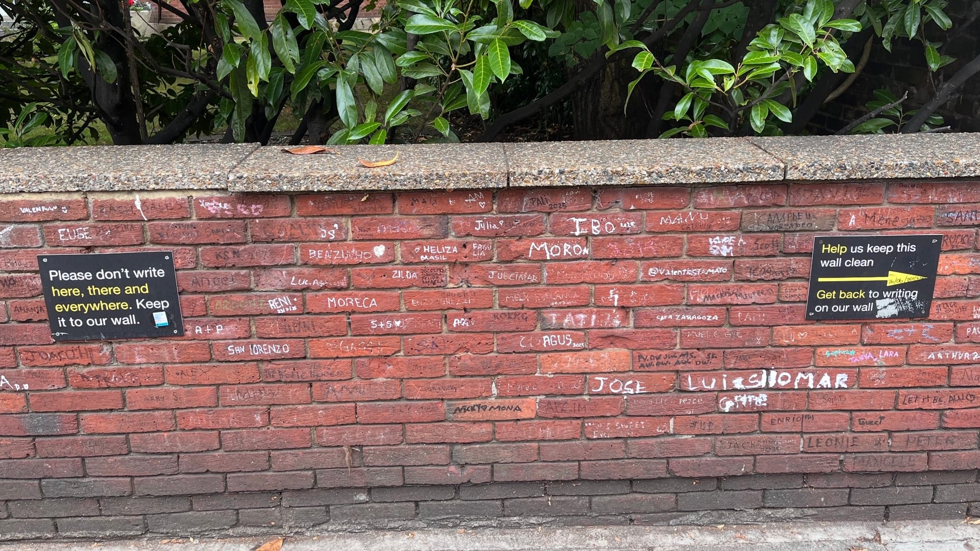 Some very clever signs on the side of Abbey Road. Reading "Please don't write here, there and everywhere. Keep it to our wall." and "Help us keep this wall clean, Get back to writing on our wall."