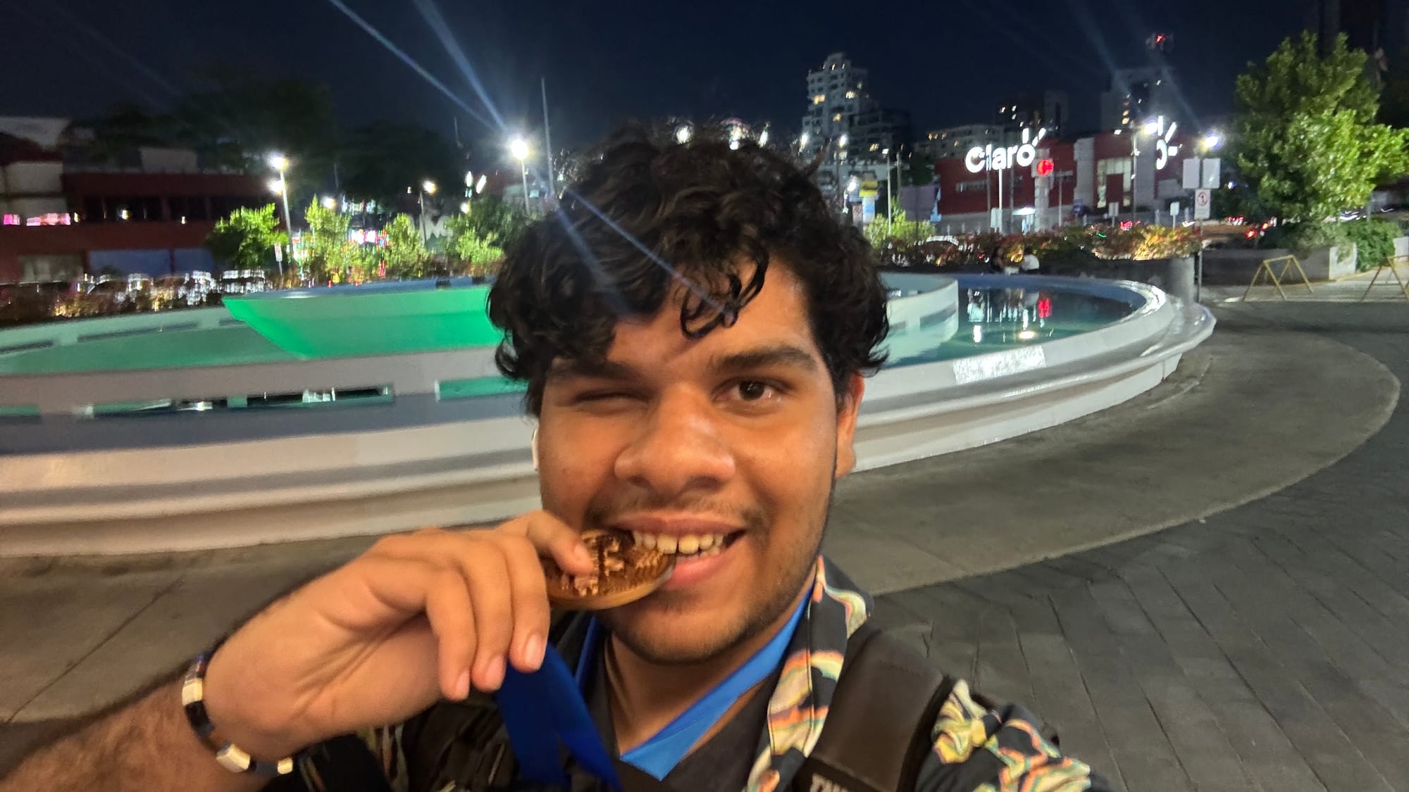 A selfie by Karl Abate, the human behind this blog, biting into his 3D-printed Bronze medal for 3BLD event in the speedcubing competition SD Summer 2026.