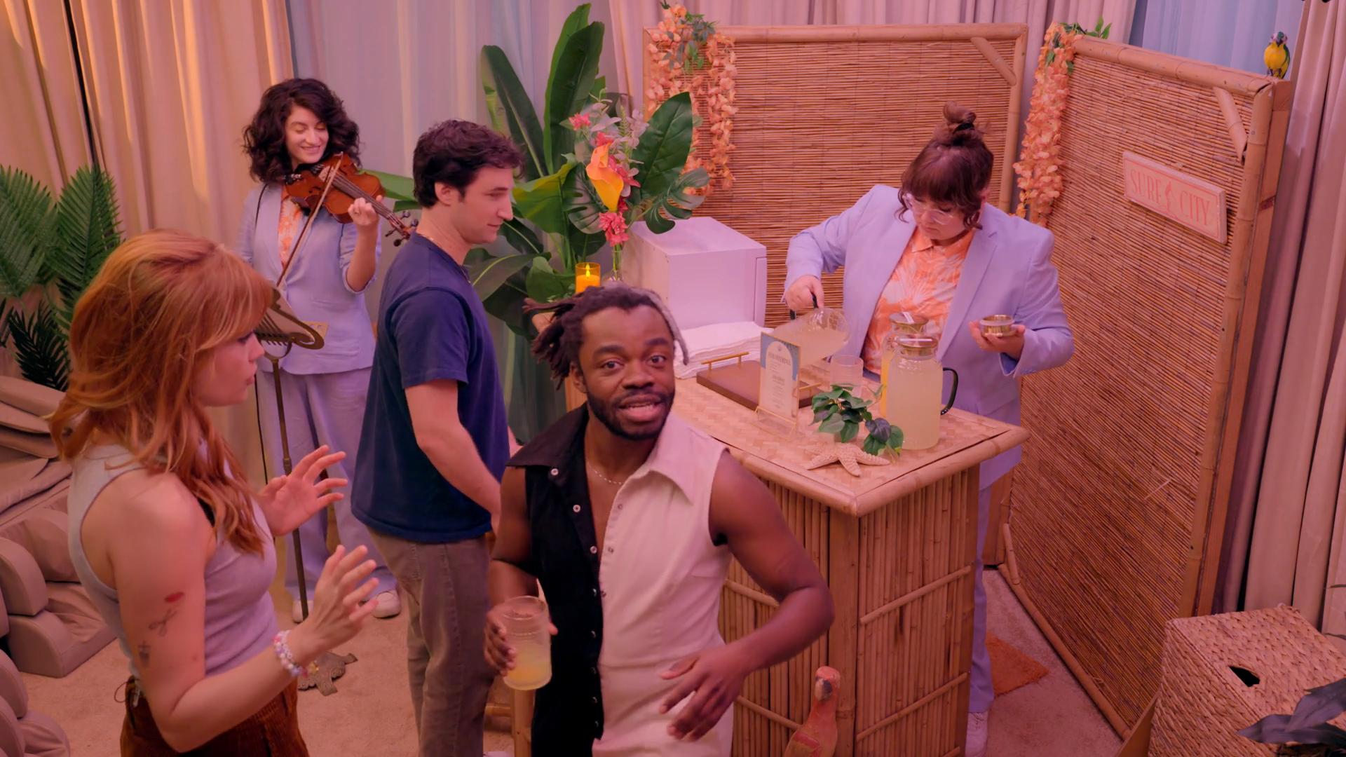 A screenshot from Game Changer S8Ep05, "Count the Rice". Catherine McCafferty, Zach Reino, and Demi Adejuyigbe are all in Loser's Island along with Jordan Myrick serving drinks, and Marina Schon playing the violin.