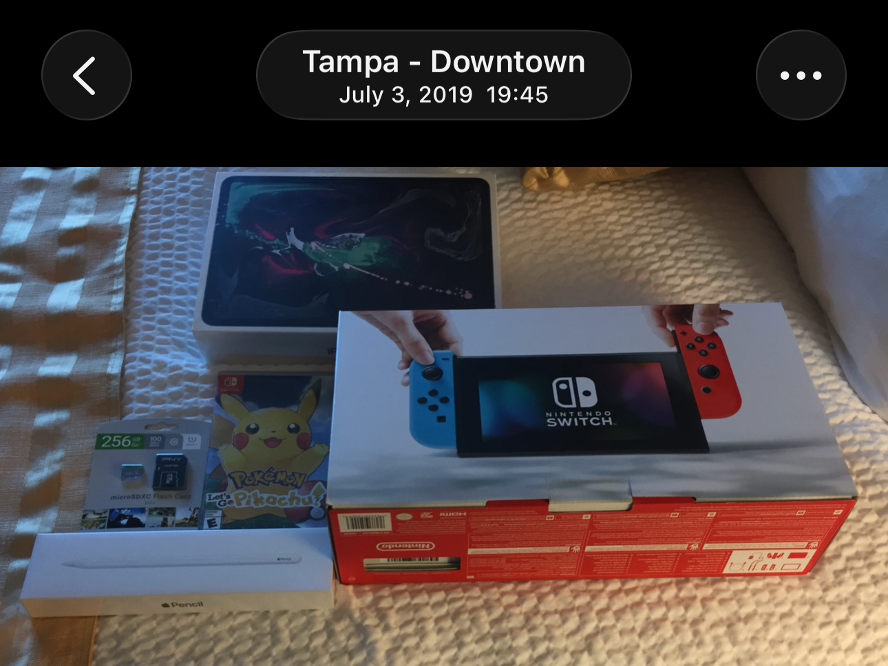 A screenshot of a photo I took on July 3, 2019, at 19:45 in Tampa, Florida. It features boxes for a 3rd Gen iPad Pro, Apple Pencil, Nintendo Switch, 256 GB Micro SD Card, and Pokémon Let's Go Pikachu!