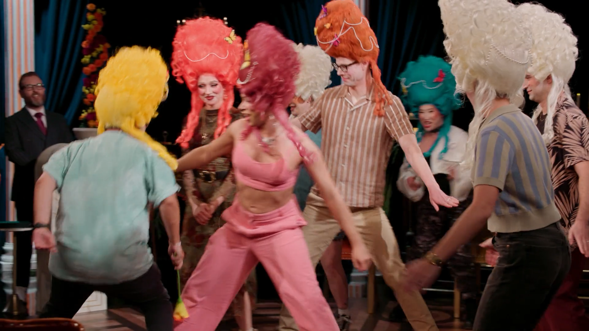 A screenshot from Game Changer S8Ep07, "Earwigs". Oscar Montoya is holding a flower that he must boop Erika Ishii with, but all the other contestants are forming a wall to protect her.