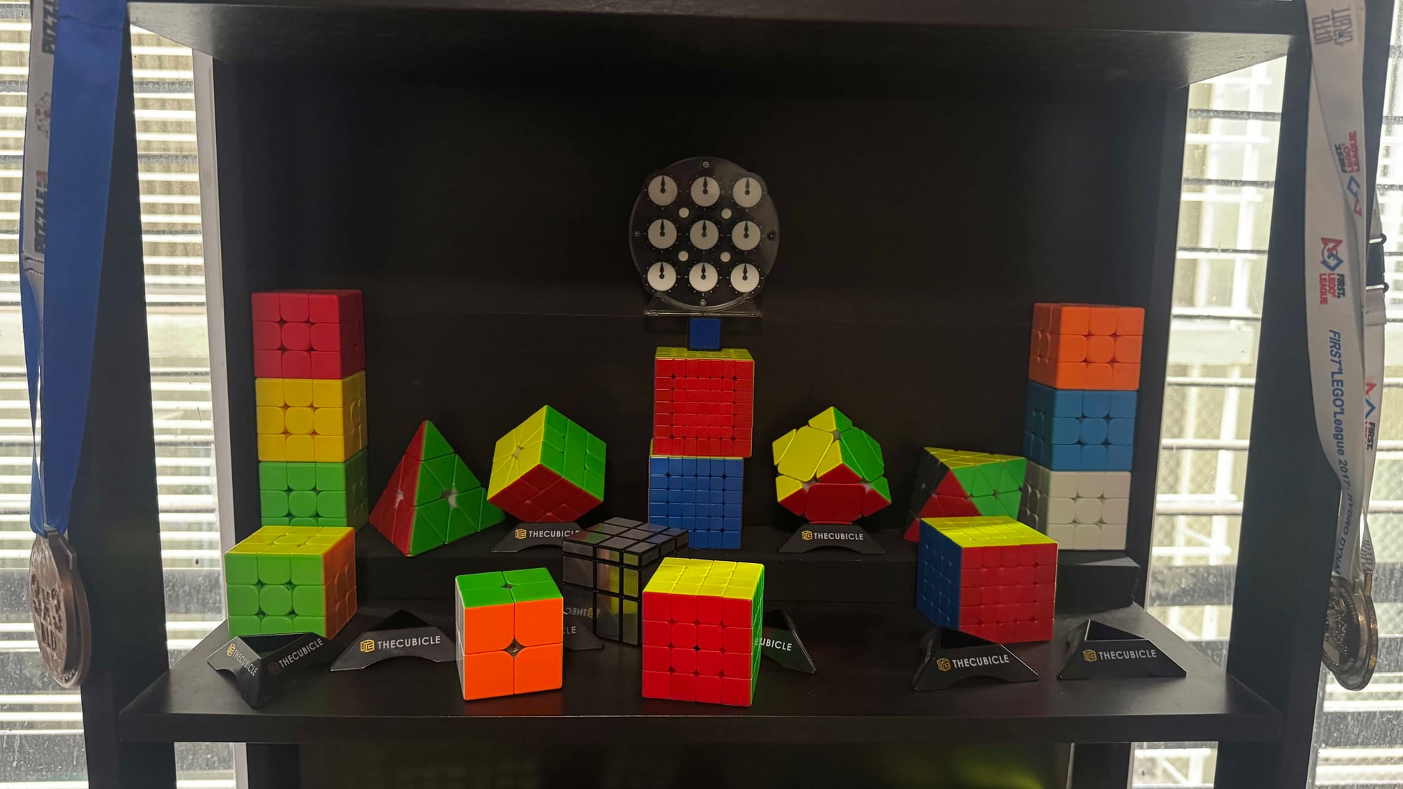 A behind the scenes photo of the previous mockup. The shelf has all the cubes scattered, an additional Mirror Blocks is there, and the clock is beind held up by a 6x6, 7x7, and 1x1 cubes.