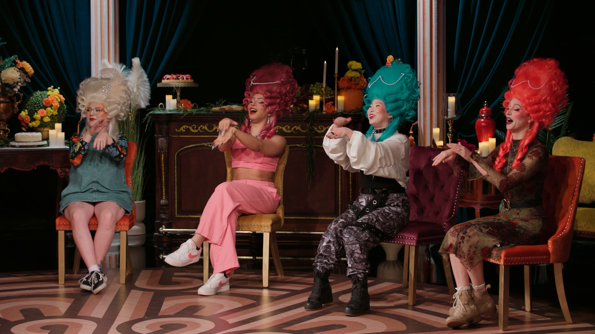 A screenshot from Game Changer S8Ep07, "Earwigs". Izzy Roland, Sephie Valentine, Erika Ishii, and Becca Scott are wearing silly wigs and applauding like decadent 18th century aristocrats.