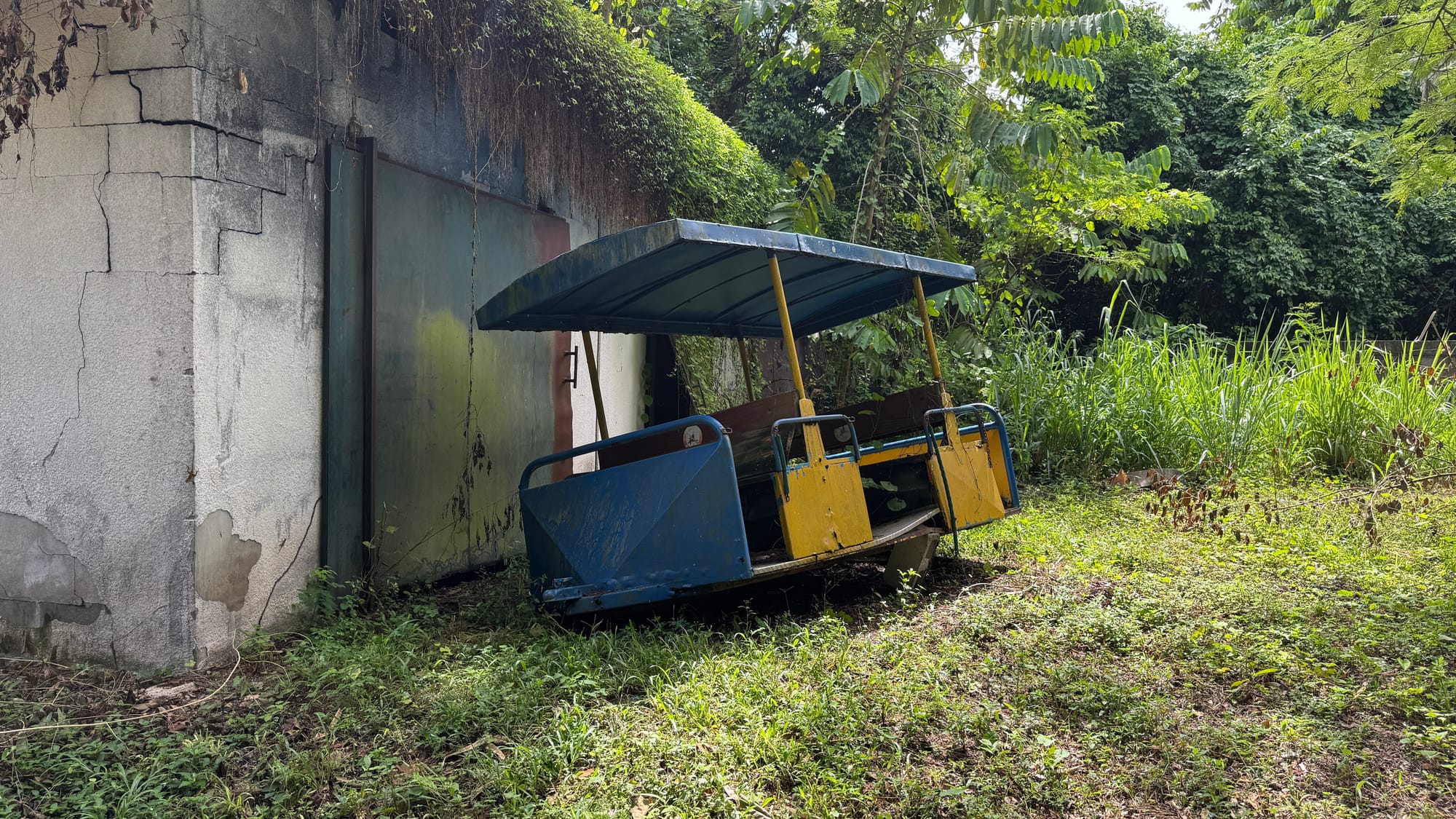 An old broken down train car from the old train at the Santo Domingo Botanical Garden. It's lying next to an unknown building.