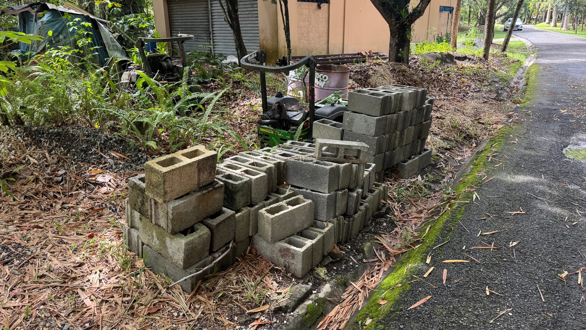 A pile of cinder blocks next to a lawnmower and some bins in the Santo Domingo Botanical Garden. They're next to an orange building.
