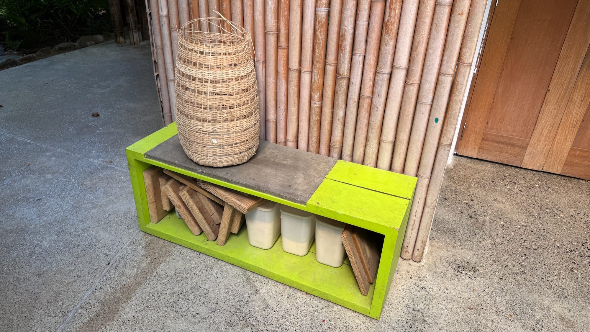 A bright lime green shelf containing a bunch of wooden planks, with a hand-woven basket on top.