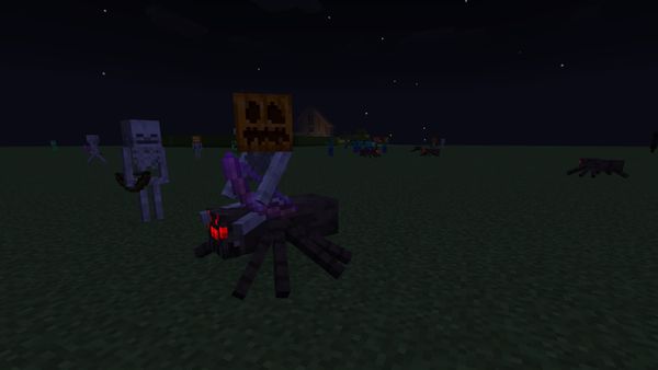 A screenshot from Minecraft, highlighting a Spider Jockey wearing a pumpkin on its head. Other zombies and skeletons are in the background also wearing pumpkins, including one with a Jack O'