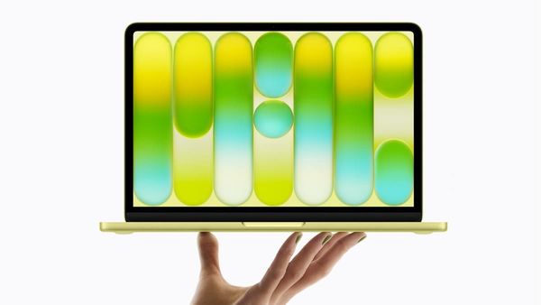 A hand holding a citrus yellow MacBook Neo. The hand also has green nails.
