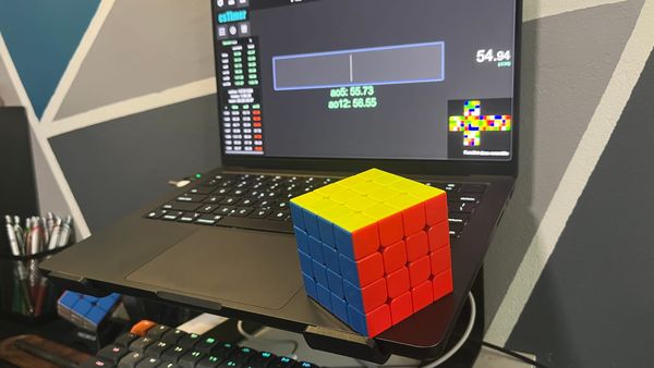 A 4x4 Rubik's Cube on top of a MacBook. It displays a most recent time of 54.94 seconds, and a personal best average of 12 of 56.55 seconds.