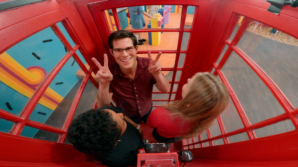 A screenshot from Game Changer S8Ep06, "Noise Some Makes", featuring Kiana Mai, Lisa Hanawalt, and Caldwell Tanner crammed together in a phone booth.