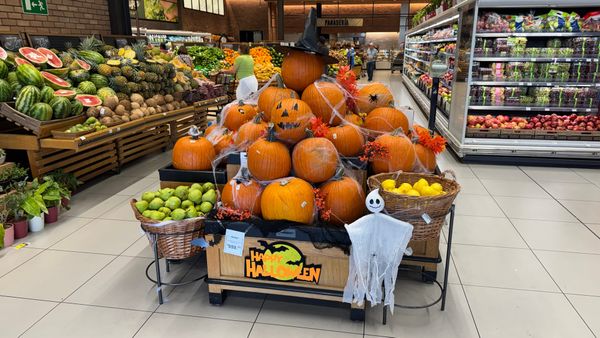 A supermarket in Santo Domingo, Dominican Republic, with a display of pumpkins at the entrance. The pumpkins are decorated with some fake cobwebs, bats, ghosts, spiders, and witch's hats.