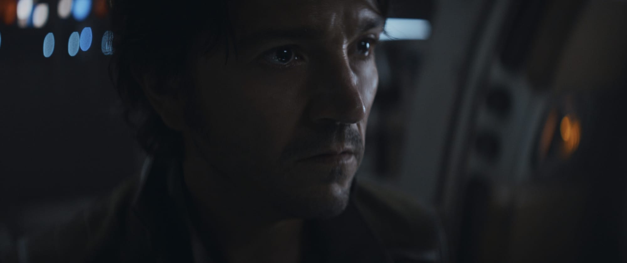 A man stands in a dark spaceship with a grim look of determination on his face.