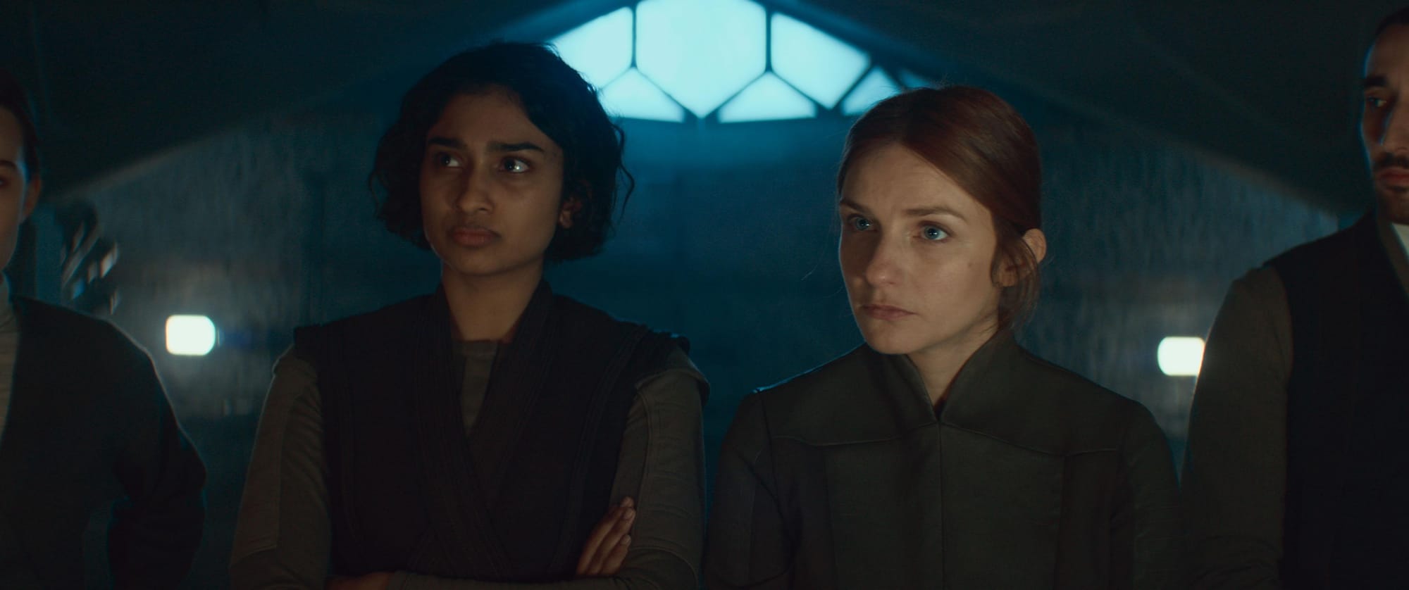 Two very tired looking rebels are standing in a dark room listening to someone off screen.