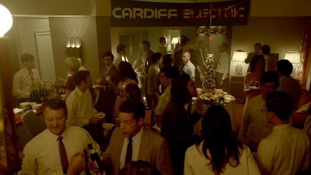 A bunch of people mill about at a party in a hotel suite. There's a shrimp tower in the midground.