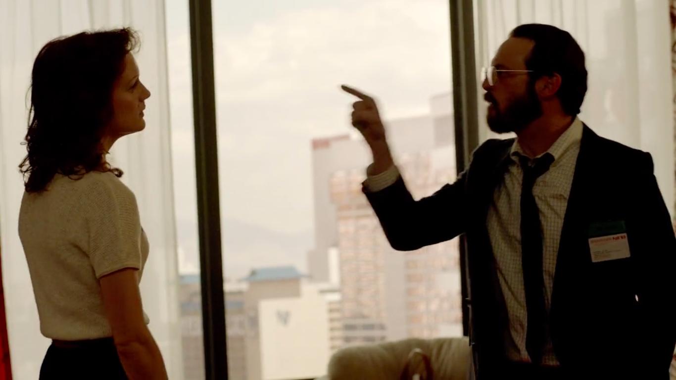 A man in a suit and tie yells at a woman in a light blouse and dark skirt.