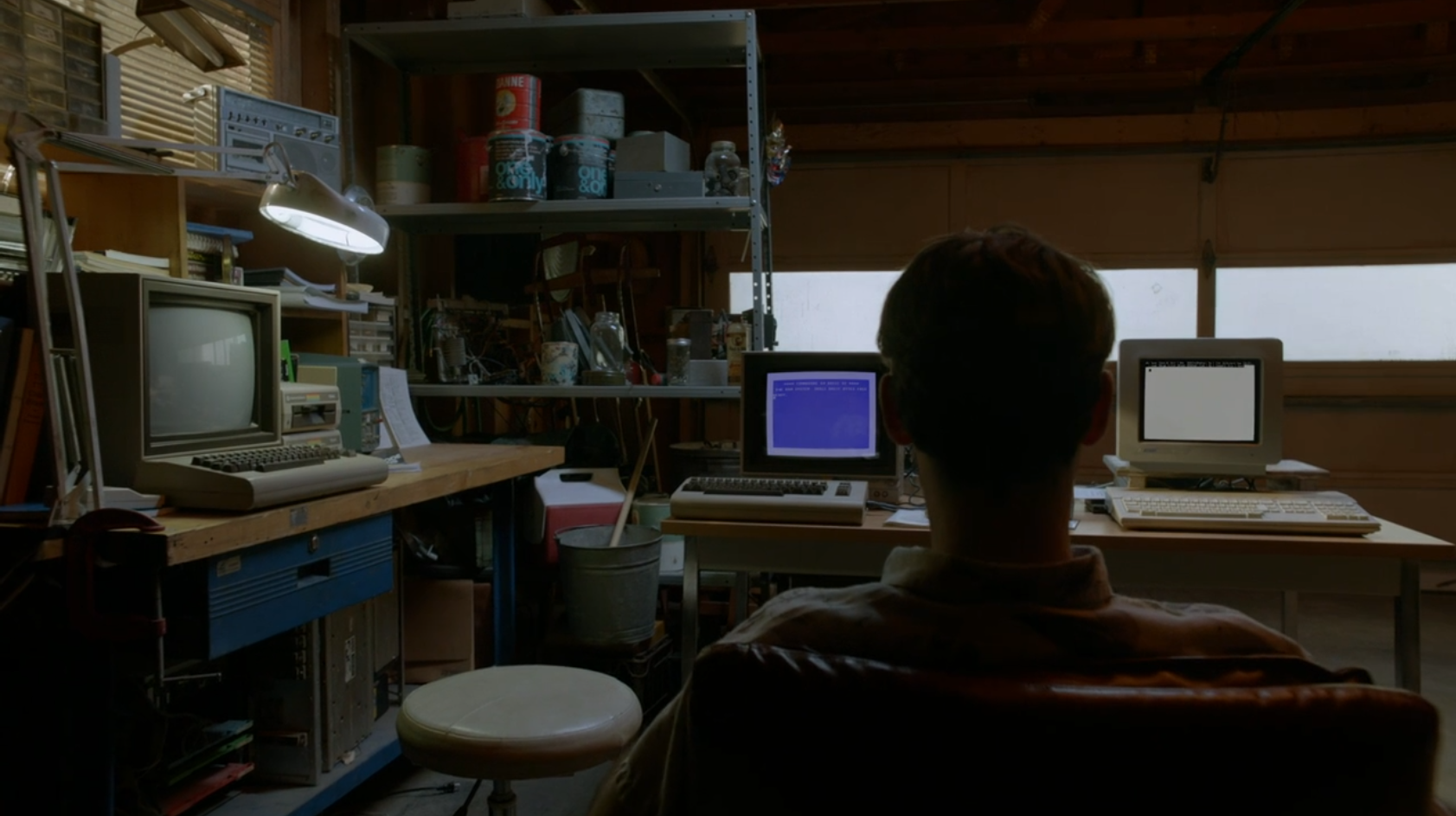 A man sits in a garage surrounded by computers.