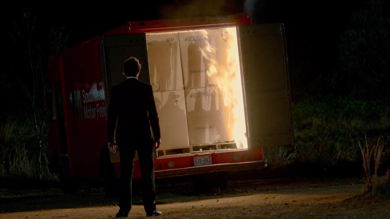 A man in a suit stands and watches a truck full of computers burn.