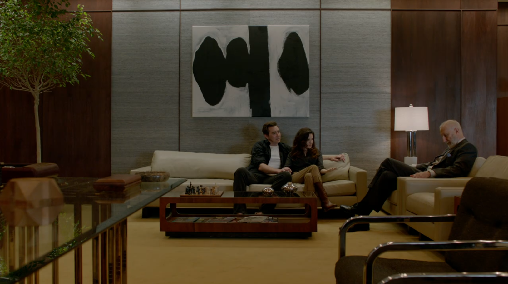 A man and a woman sit on a couch and tell something to an older man sitting in a chair perpendicular from them.
