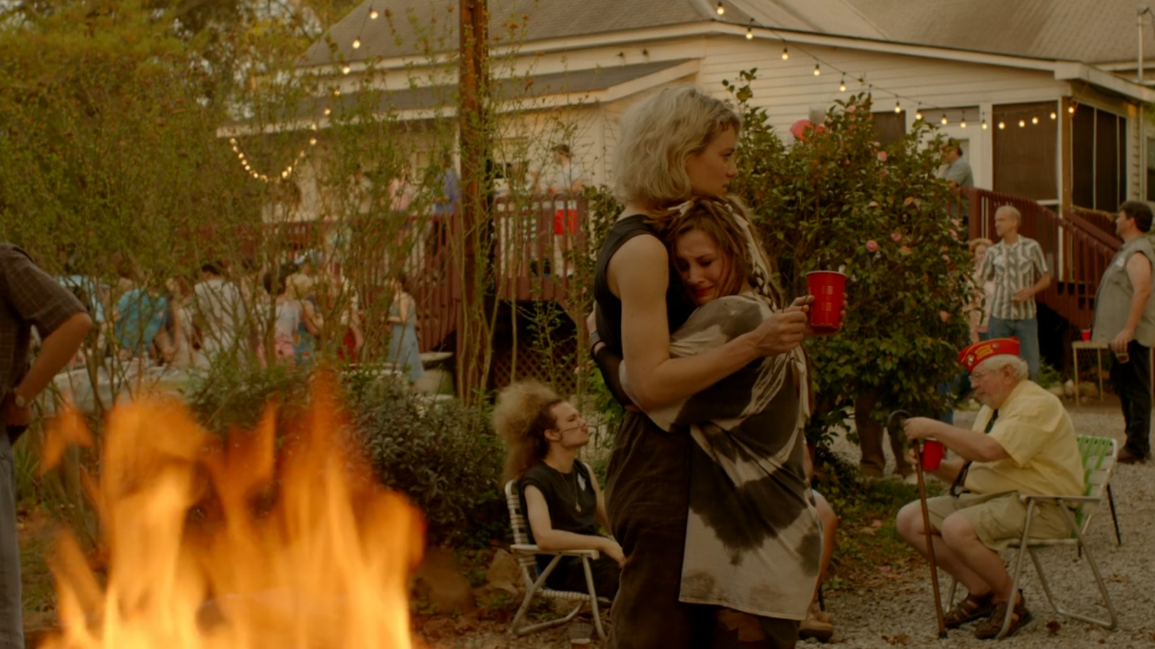 A young woman with dyed blonde hair is hugged by a shorter young woman with messy brown hair.