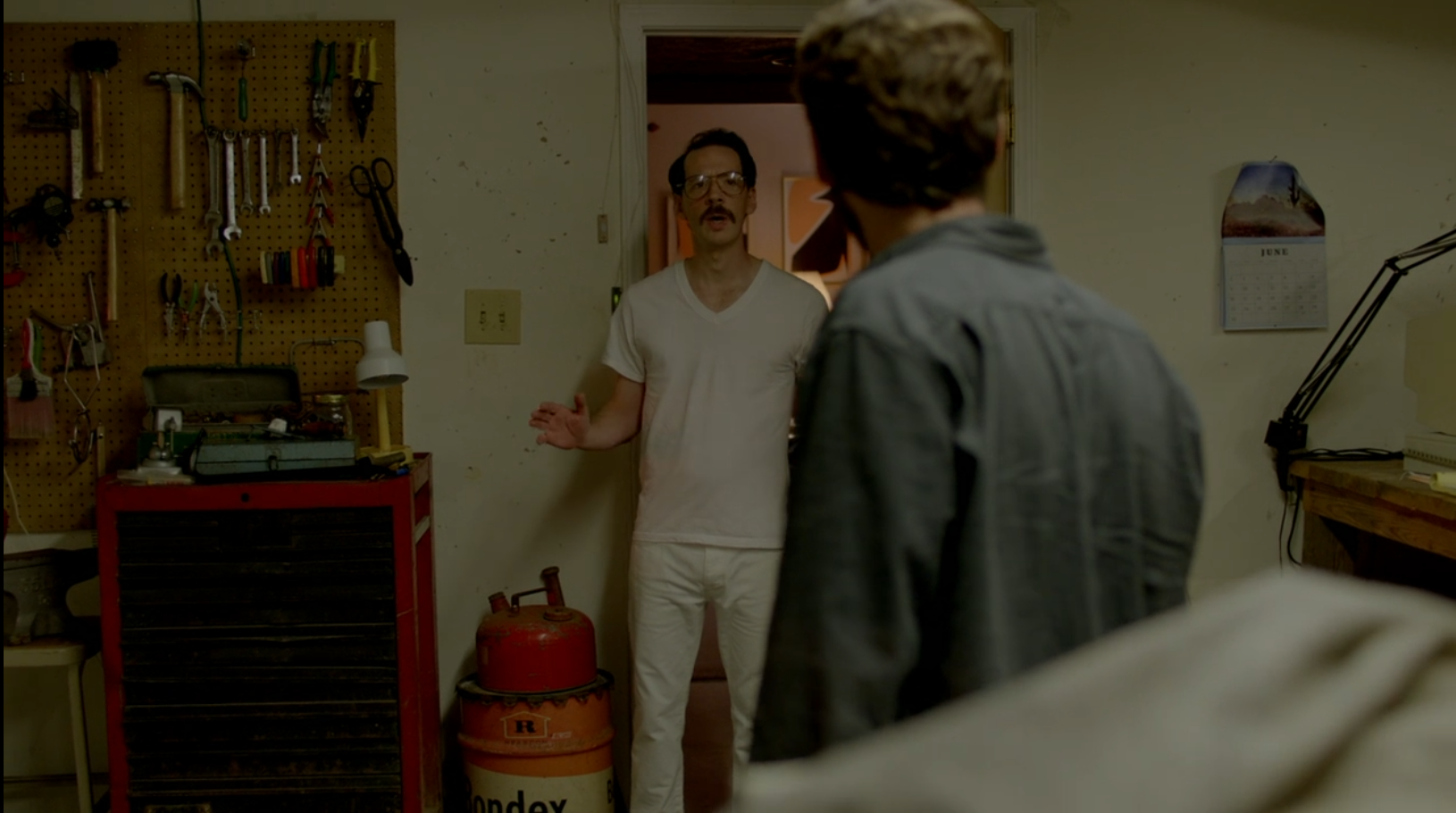 A man in white pajamas confronts another man in his garage.