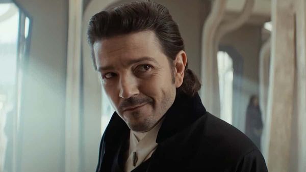 Cassian Andor (Diego Luna), in disguise as a merchant, looks at someone offscreen in a hotel lobby on Ghorman 