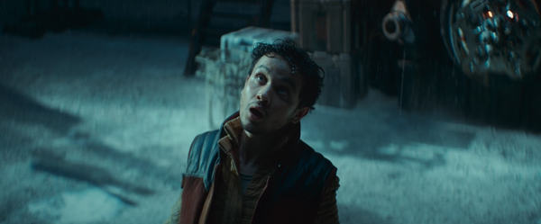 A young man in an orange and black jacket stands in snow in front of a fuel depot breathing in dangerous fumes.