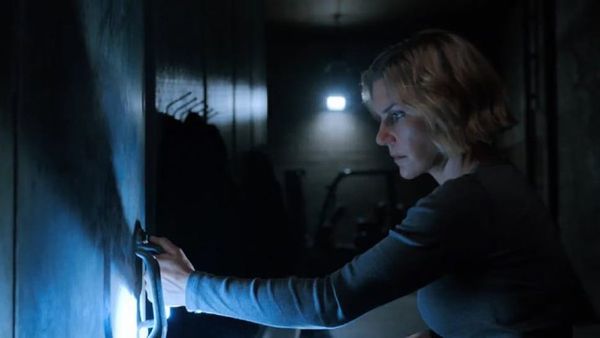 A woman, in a dark facility of some kind, looks determined to open a walk-in refrigerator unit. 